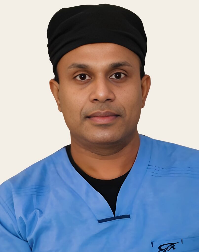 A man wearing a dark surgical cap and blue medical scrubs, looking directly at the camera against a light background.