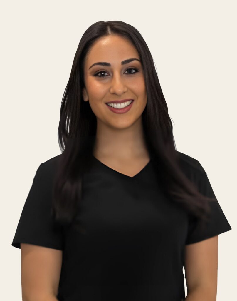 A woman smiling in a black v-neck shirt against a light beige background. Her long dark hair frames her face, and she appears professional and approachable.